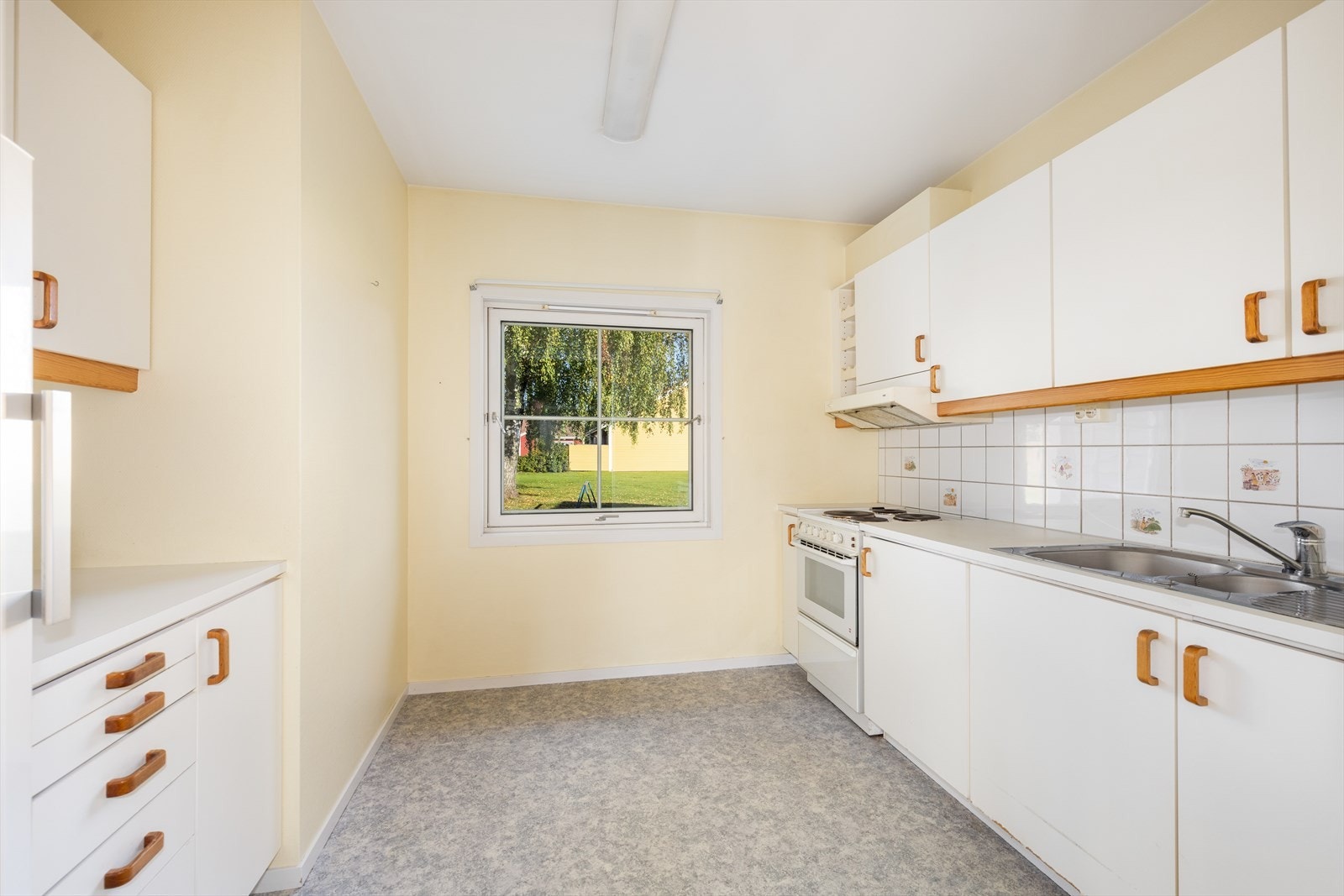 Kjøkkenet har innredning på begge sider av rommet, med slette fronter og benkeplate i laminat med flis over. Over stekesone er det ventilator med avtrekk ut. Galleribilde