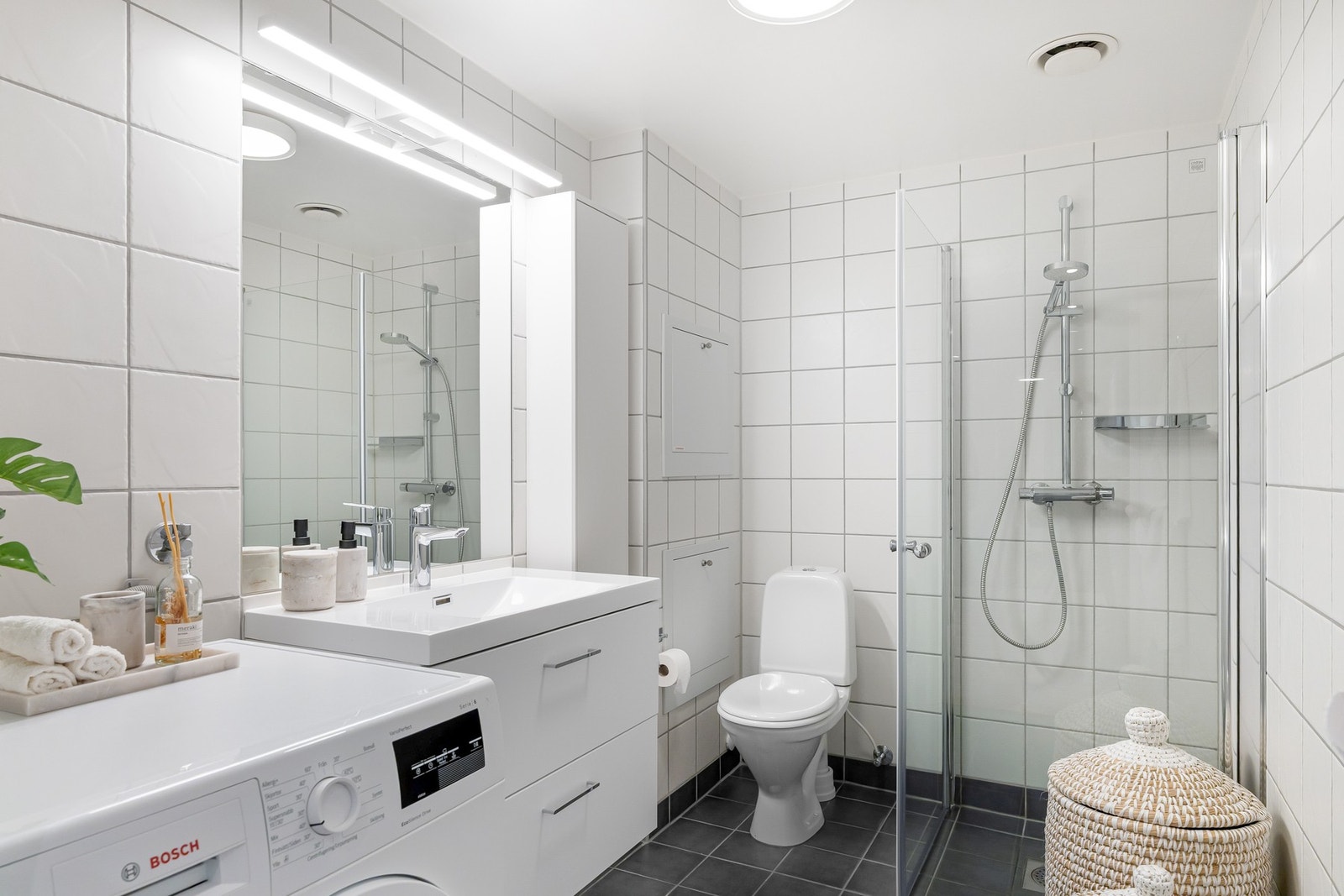 Badet er innredet med dusjhjørne, gulvmontert toalett, samt servantseksjon med skuffer og speil. Galleribilde