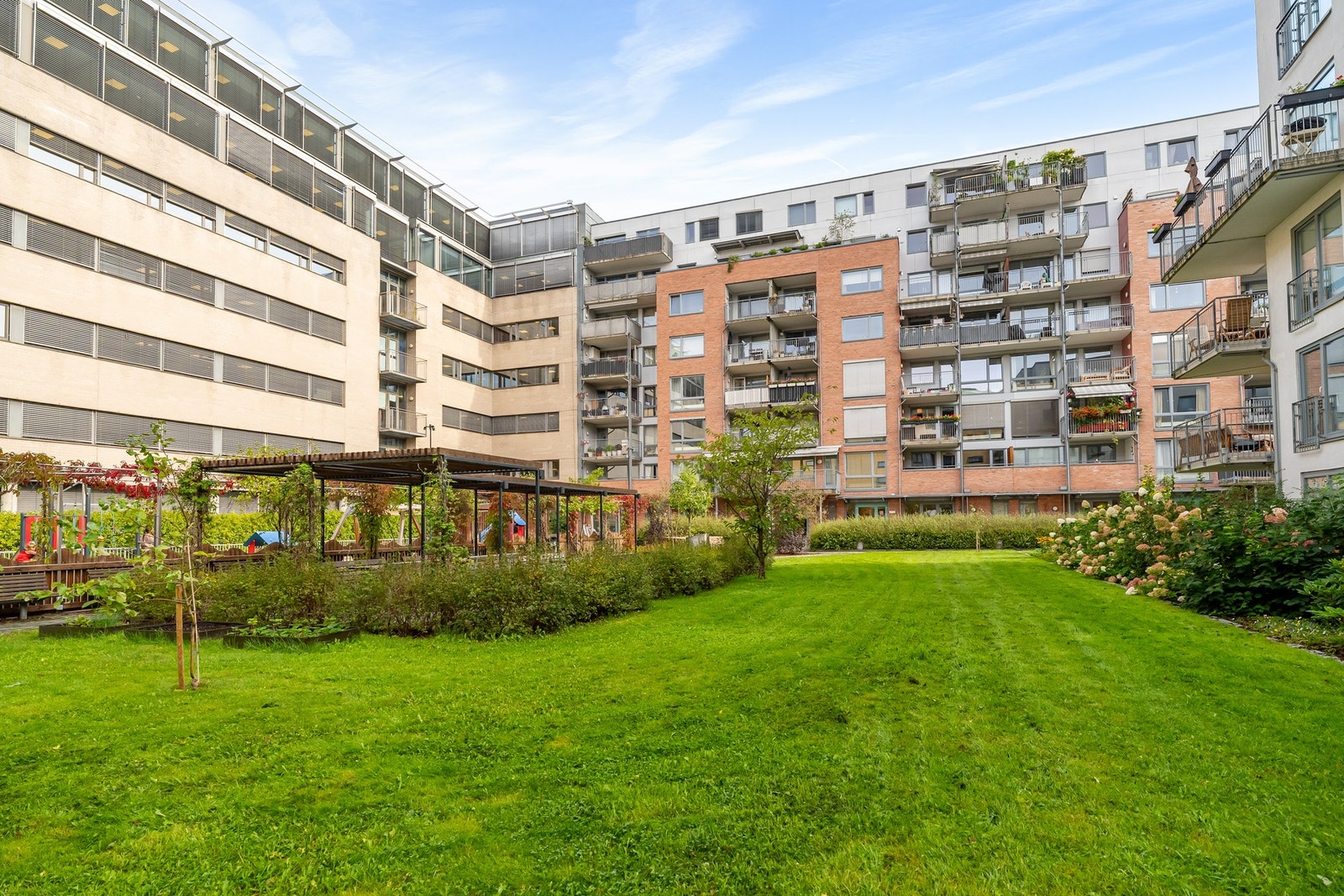 Pent opparbeidet bakgård, skjermet og solrikt med gressplener, frodig beplantning og hyggelige sittegrupper. Galleribilde