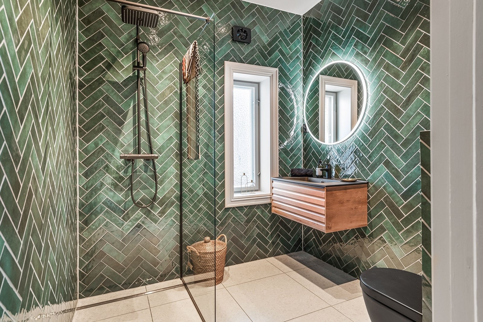 Badet fremstår som svært innbydende, med store lyse gulvfliser som gir en følelse av rom og eleganse, kombinert med dekorative fiskebensfliser på veggene i en delikat grønntone Galleribilde