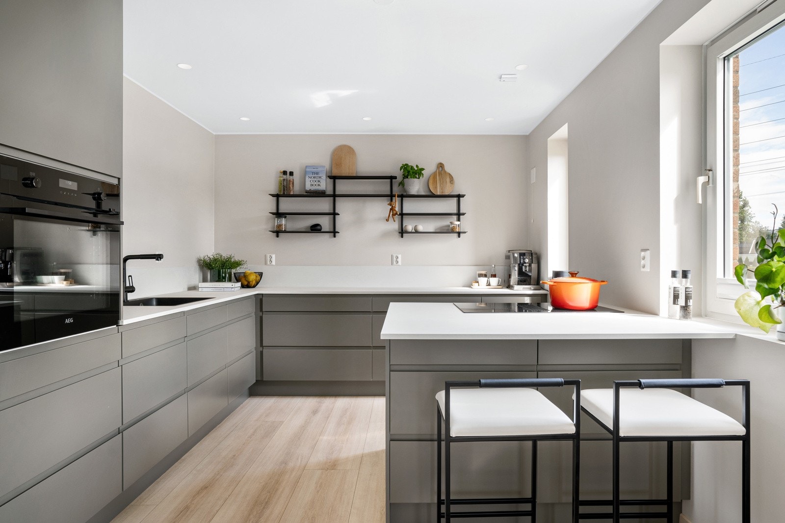 Kjøkkeninnredning fra Huseby med integrerte grep og en stilig backsplash i lyse nyanser. For et luftigere uttrykk er overskap droppet til fordel for åpne flater og hyller, men det er likevel rikelig med oppbevaringsplass i skuffer. Galleribilde