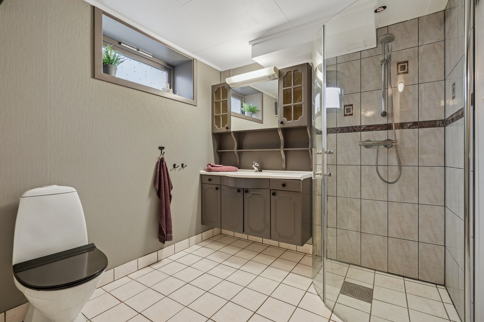 Badet har flislagt gulv m/gulvvarme og malerstrie på vegger - Rommet er utstyrt med dusjhjørne m/glassvegger, toalett og baderomsinnredning Galleribilde