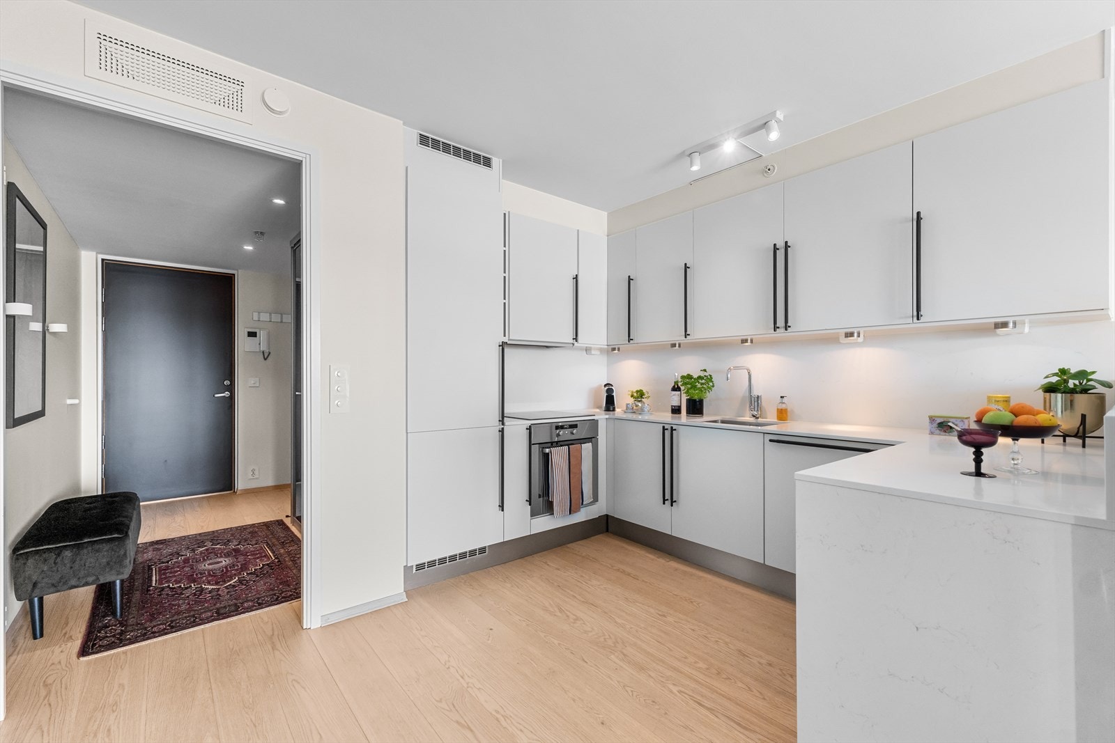Lyst og moderne kjøkken med slette fronter, integrerte hvitevarer og downlights. Galleribilde