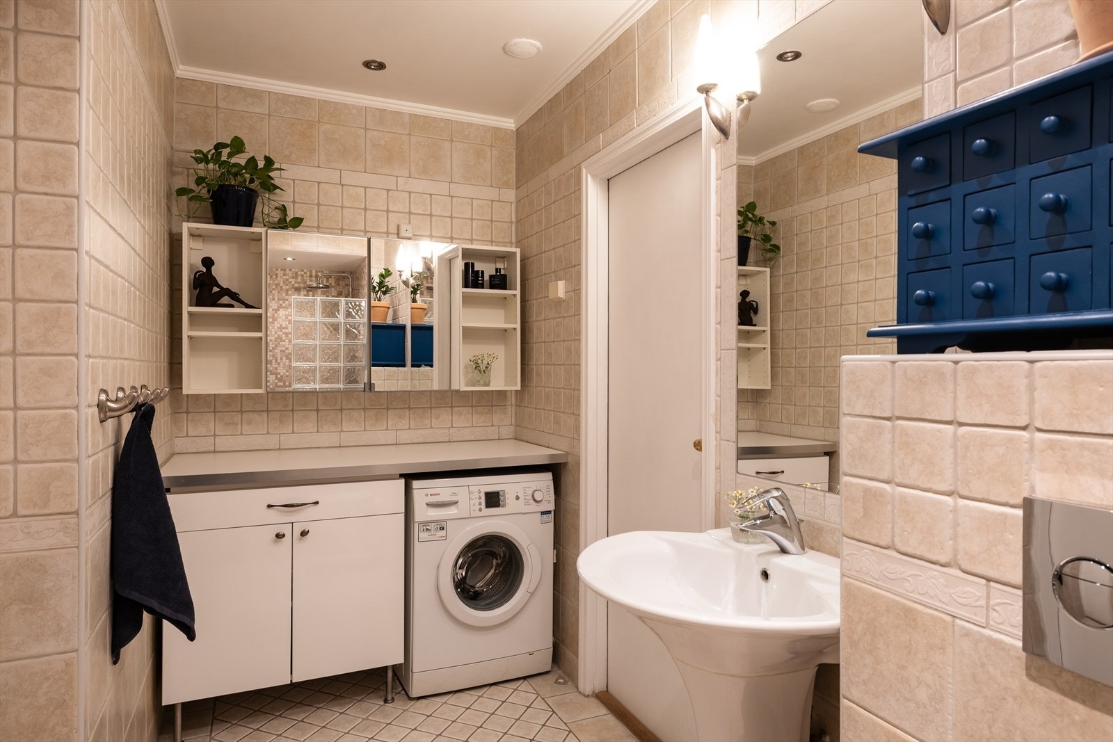 Delikat baderom med delikate fliser og praktiske løsninger. Praktisk benkeløsning med opplegg for vaskemaskin under. Galleribilde