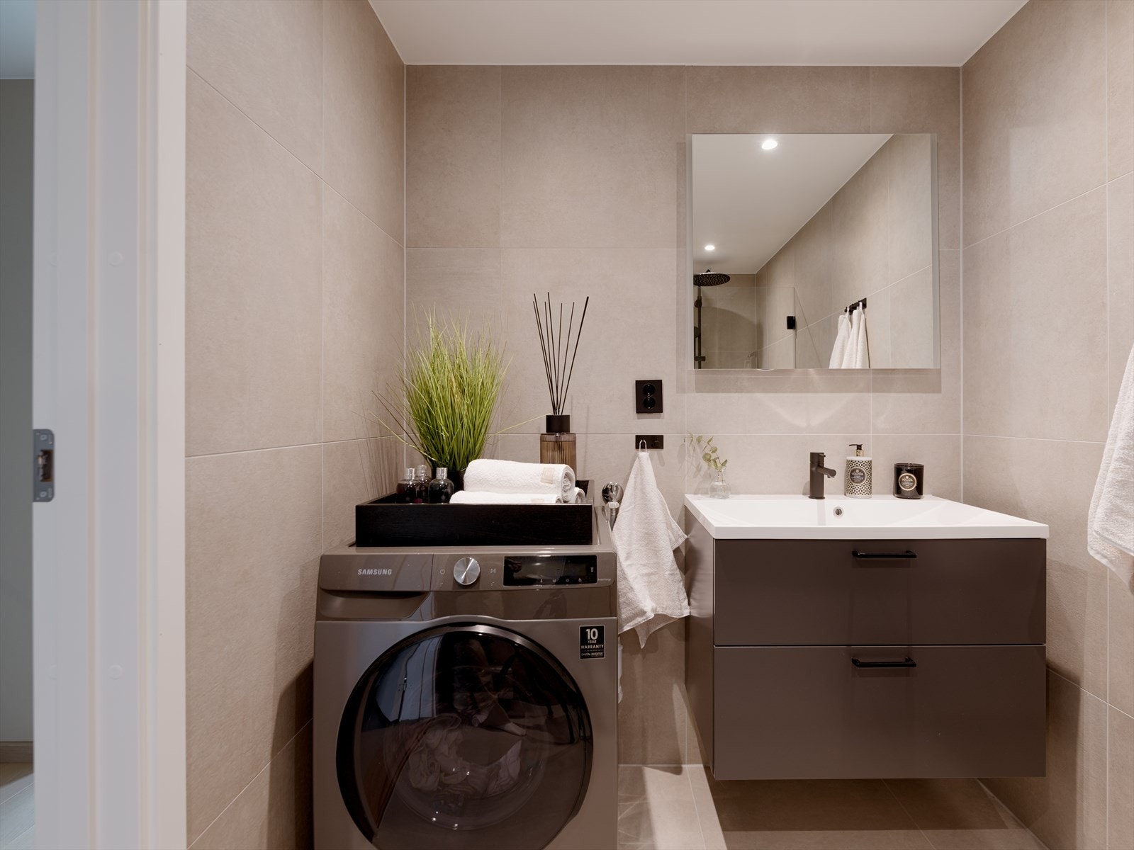 Badet består av heldekkende servant på underskap med folierte fronter, speil, lysarmatur, veggmontert klosett, samt dusjhjørne. Galleribilde