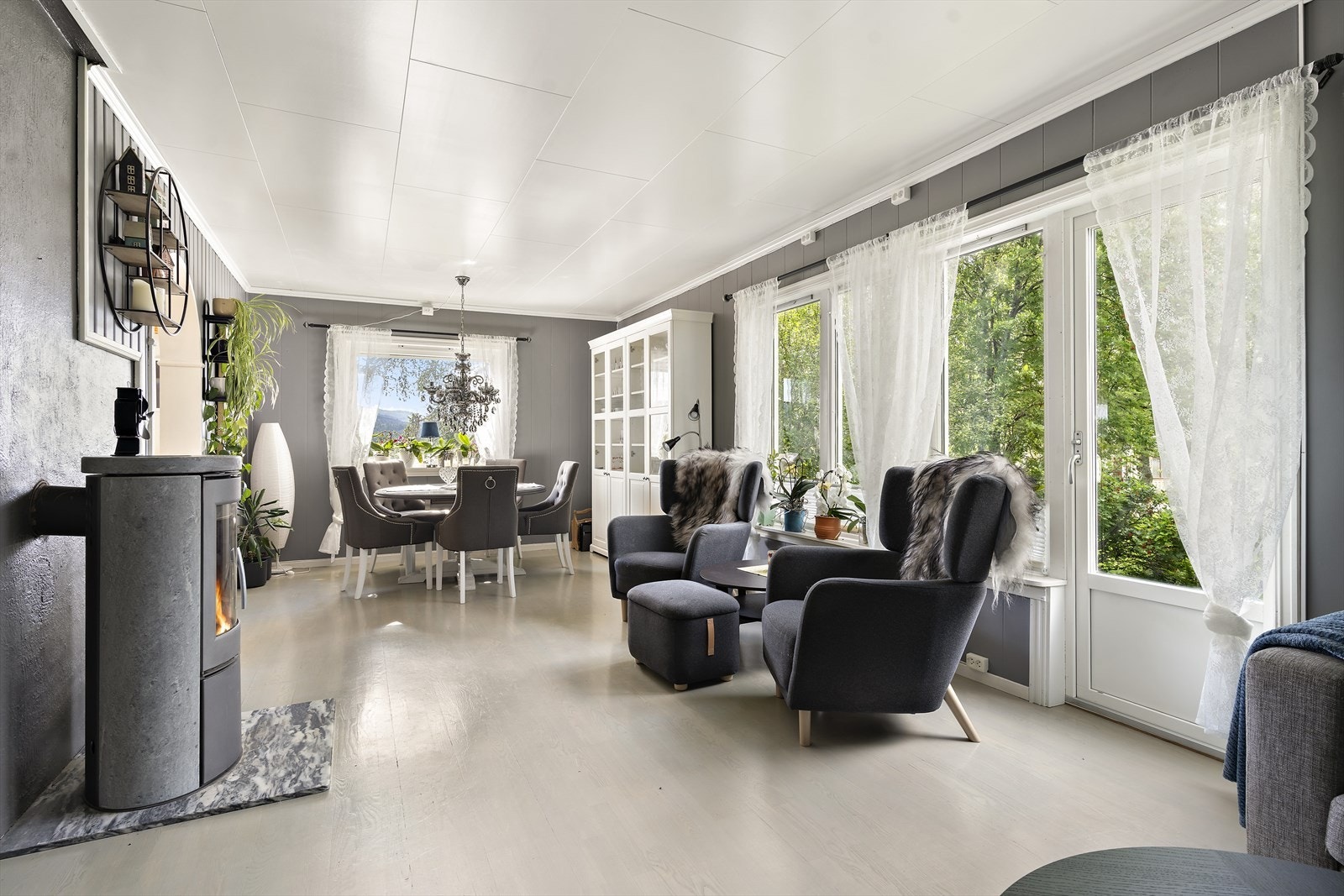 Koselig stue som får godt med dagslys inn gjennom vindusflatene. Vedovnen er fra 2020 og sørger for både varme og hyggelig stemning. Fra verandadøren har du trapp ned til plenen. Galleribilde