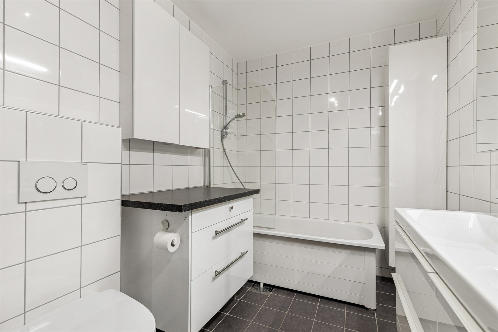 Bad fra byggeår. Flislagt gulv med gulvvarme og flislagte vegger. Malte flater i himling. Vegghengt servantinnredning med skuffer. Dobbel ovenpåliggende servant med ett-greps armaturer. Galleribilde