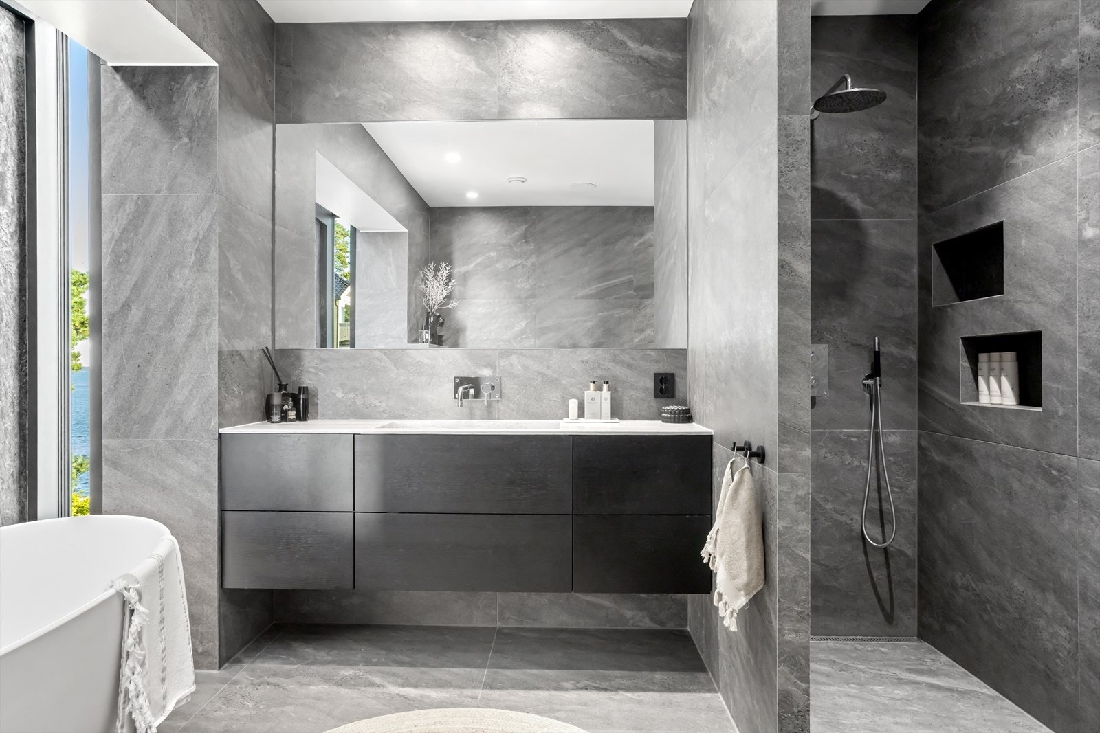 Legg merke til den flotte baderomsinnredningen fra Svane. Her bys det på elegant servantbenk i stein og integrert blandebatteri. Massevis av kolonialskuffer med mørke fronter gir god oppbevaringsplass og viderefører kvalitetsinntrykket. Galleribilde