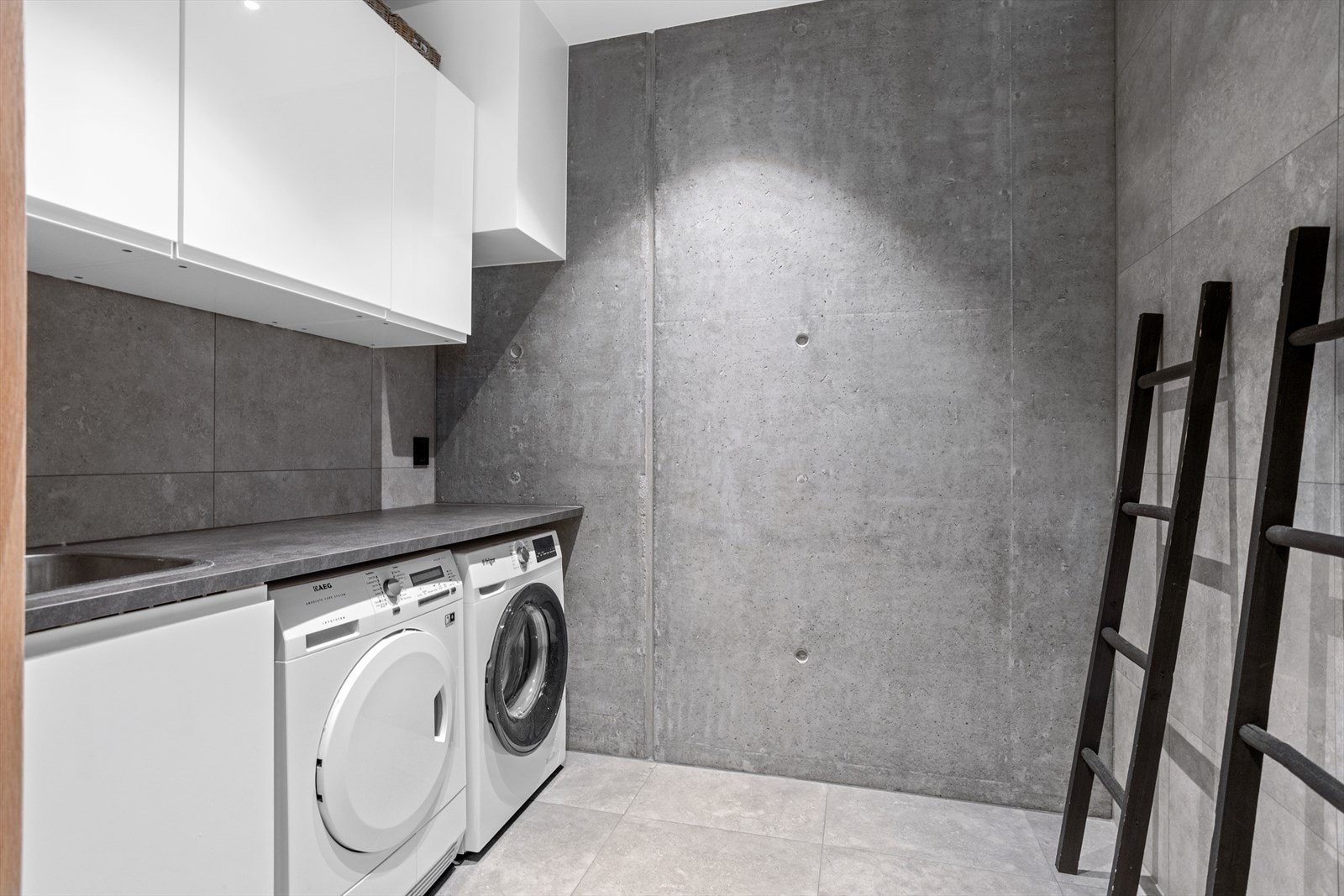 Vaskerommet ligger innenfor baderommet i 1. etasje, skyvedør holder rommene adskilt. Det er benyttet ellers like gulv-/veggfliser som på baderommet for å ivareta helhentsfølelsen. På vaskerommet er det også eksponert betongvegg. Galleribilde