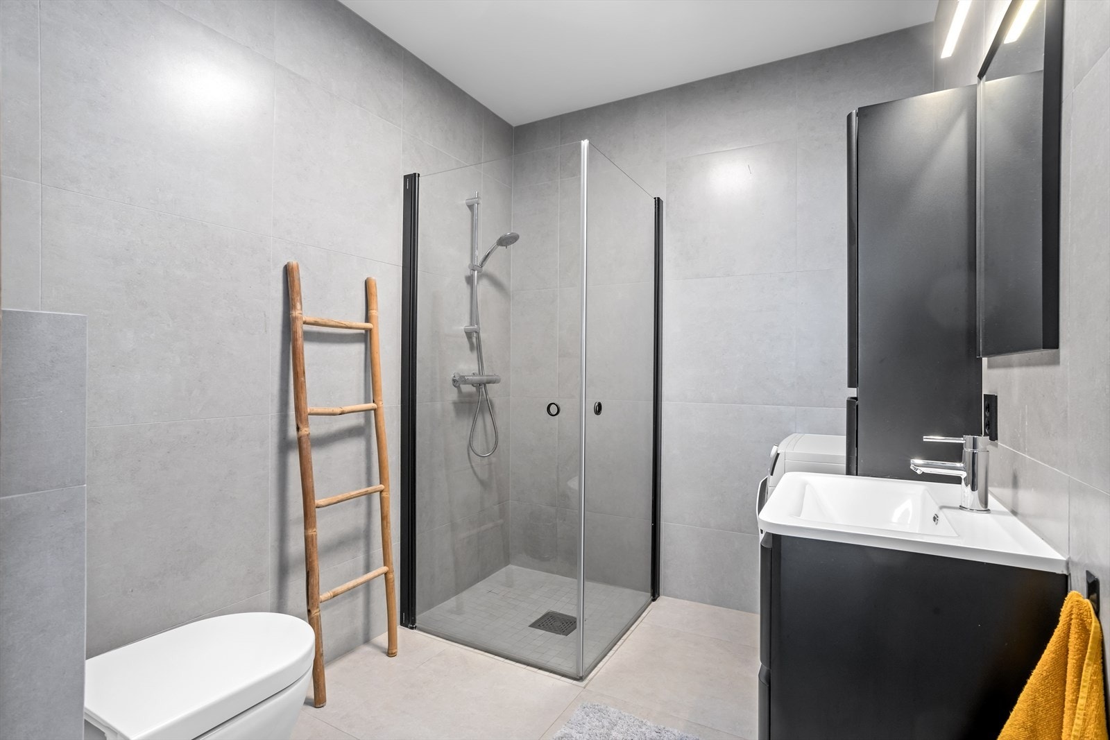 Også baderommet her har store og moderne fliser med matte overflater hvor store dimensjoner forsterker den moderne følelsen. Det er dusjhjørne med dører av herdet glass og noe nedsenket gulv med fliser av mindre dimensjon enn øvrige gulvfliser. Galleribilde