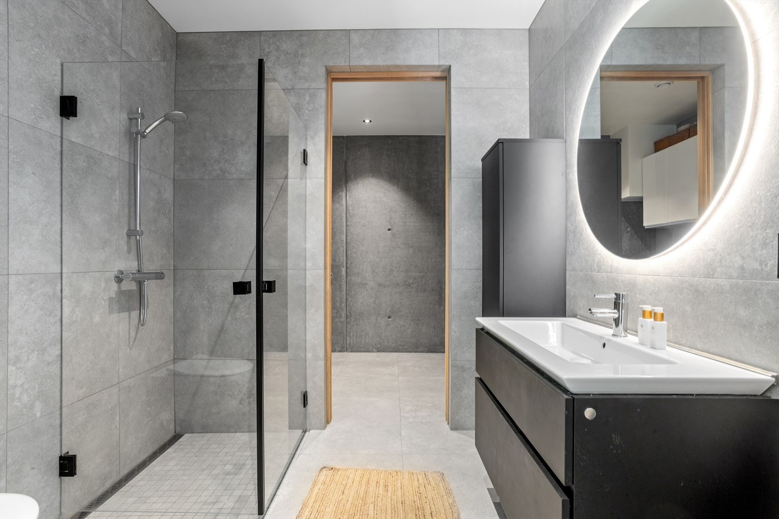 Også på baderommet i 1. etasje dominerer de store og svært moderne gulvflisene. Flisenes matte overflater og store dimensjoner forsterker den moderne følelsen. Badet er innredet med dusjhjørne med dører av herdet glass og "rennesluk" innerst i dusjen. Galleribilde