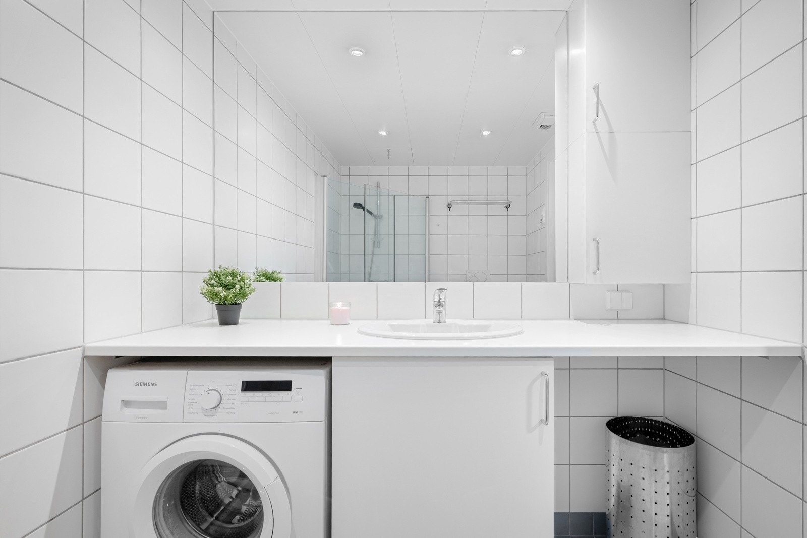 Baderommet har servant, speil, dusjhjørne, vegghengt skap, vegghengt toalett og opplegg for vaskemaskin. Galleribilde