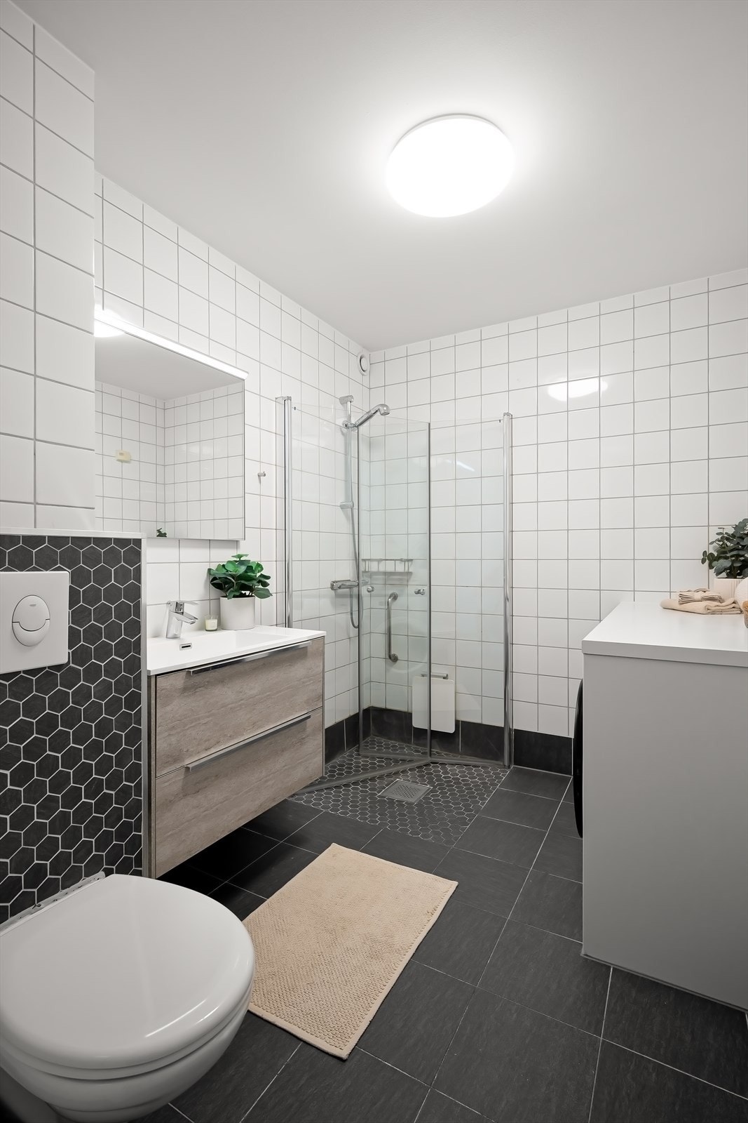 Pent helfliset baderom fra 2018 utstyrt med servant og servantskap, veggmontert wc, opplegg for vaskemaskin, dusjhjørne med innfellbare dusjdører Galleribilde
