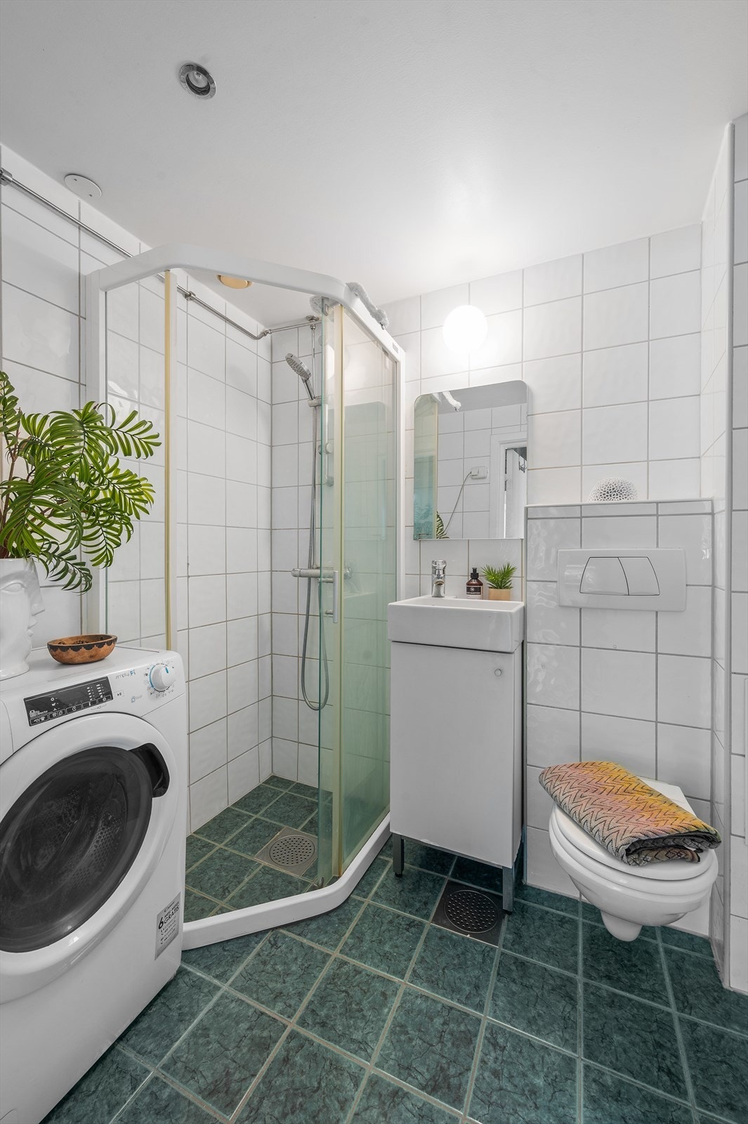 Videre har badet dusjhjørne med skyvbare glassdører og vegghengt klosett. Det er opplegg for vaskemaskin. Galleribilde