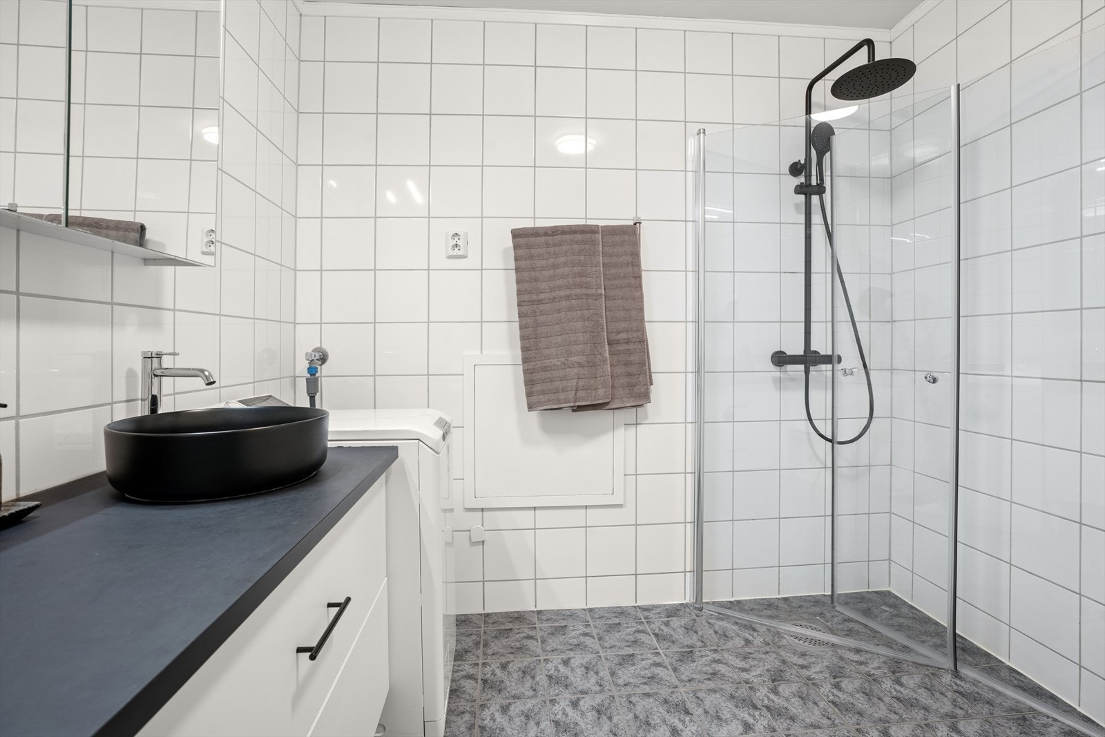 Pent dusjhjørne med glassdører. Det er opplegg for vaskemaskin og ventilasjon gjennom avtrekksvifte i himling. Galleribilde
