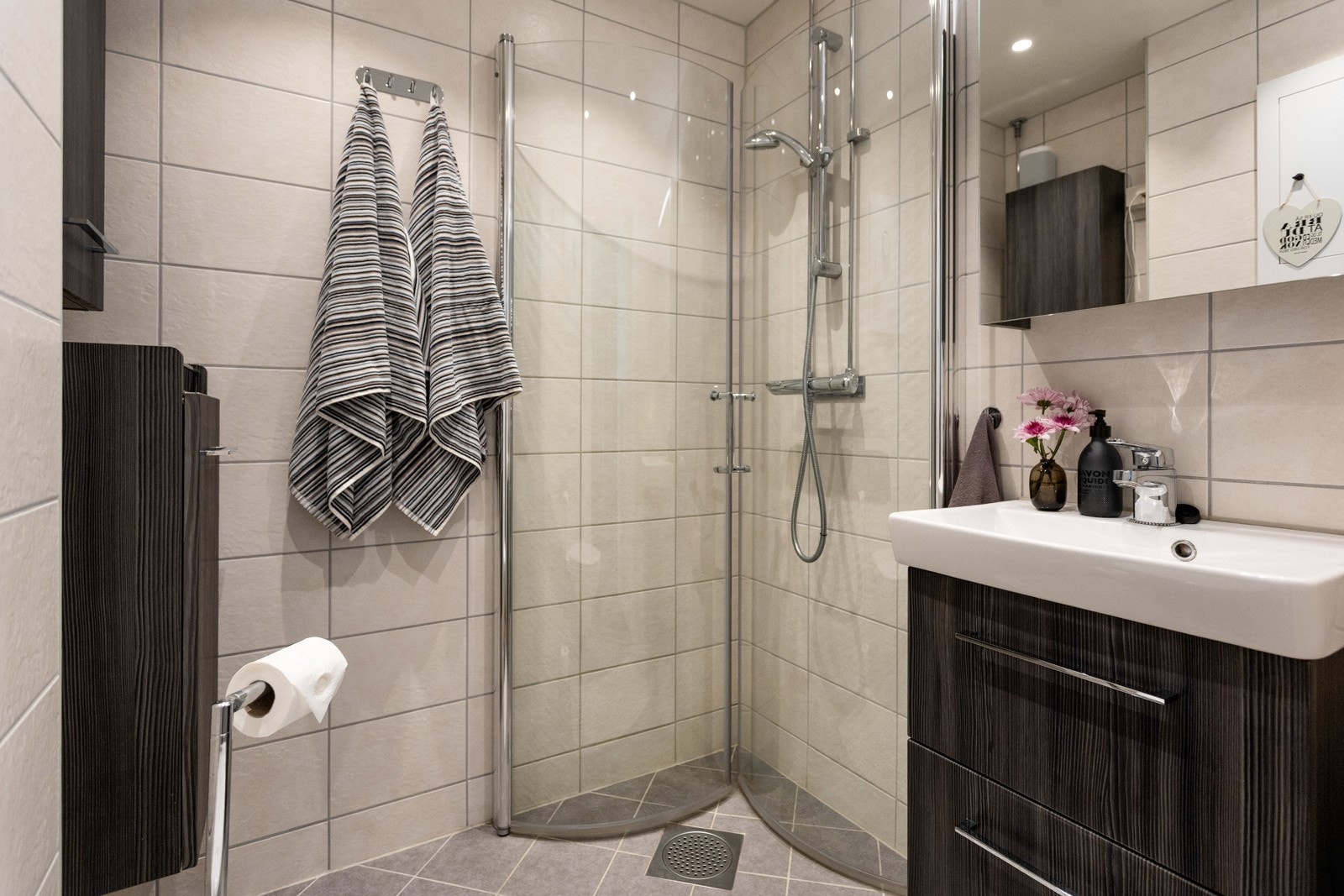 Baderommet(2021) er moderne og delikat, med fliser på både gulv og vegger. Rommet er utstyrt med et stilrent servantskap, vegghengt speil med belysning, samt dusjhjørne med innfellbare glassdører. Galleribilde