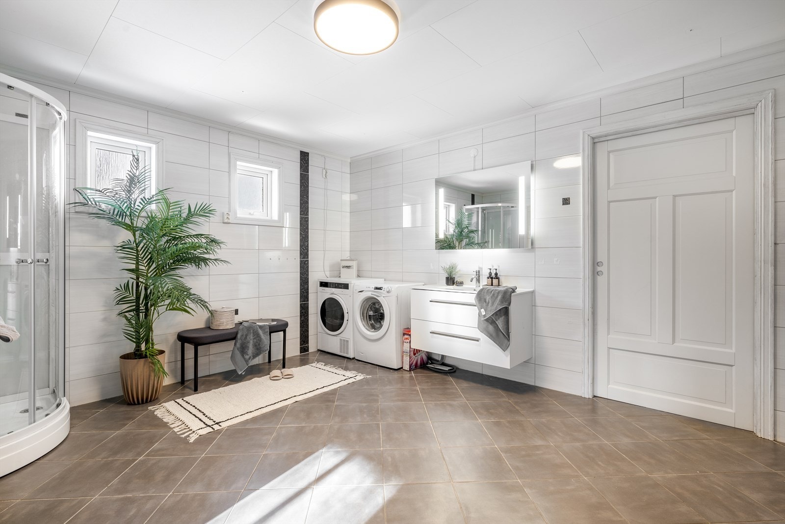 Badet har flis på gulv og vegger, og inneholder toalett, tett dusjkabinett (2023) og innredning med heldekkende hvit vask, underskuffer med slette fronter og speil med lys.
Balansert ventilasjonsanlegg. Ventil i tak og luftespalte i dør. Galleribilde