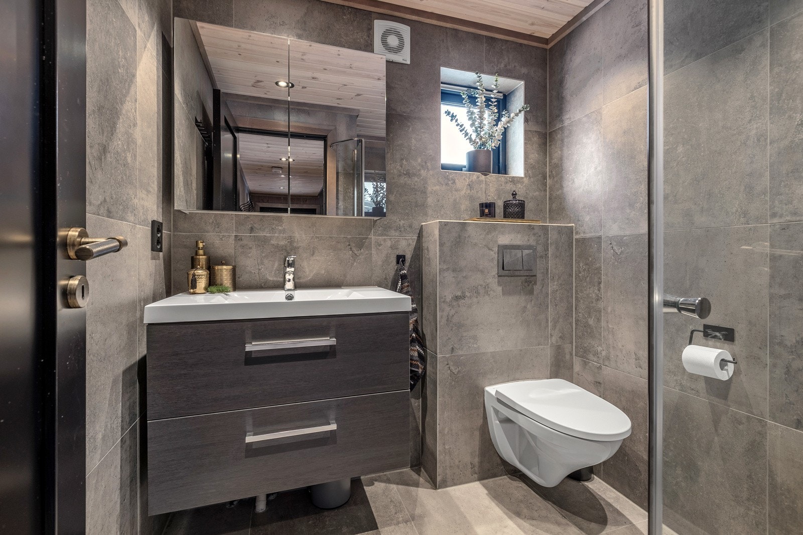 Lekkert baderom med nedfelt servant, veggmontert toalett og dusjhjørne. Speilskap over servant og servantskap med skuffer gir god plass til oppbevaring. Galleribilde