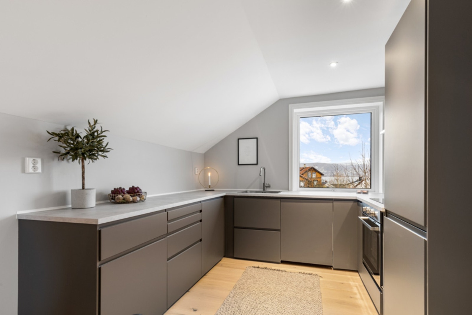 Slette, grå fronter med innfreste gripetak er kombinert med lyse benkeplater i laminat. Galleribilde