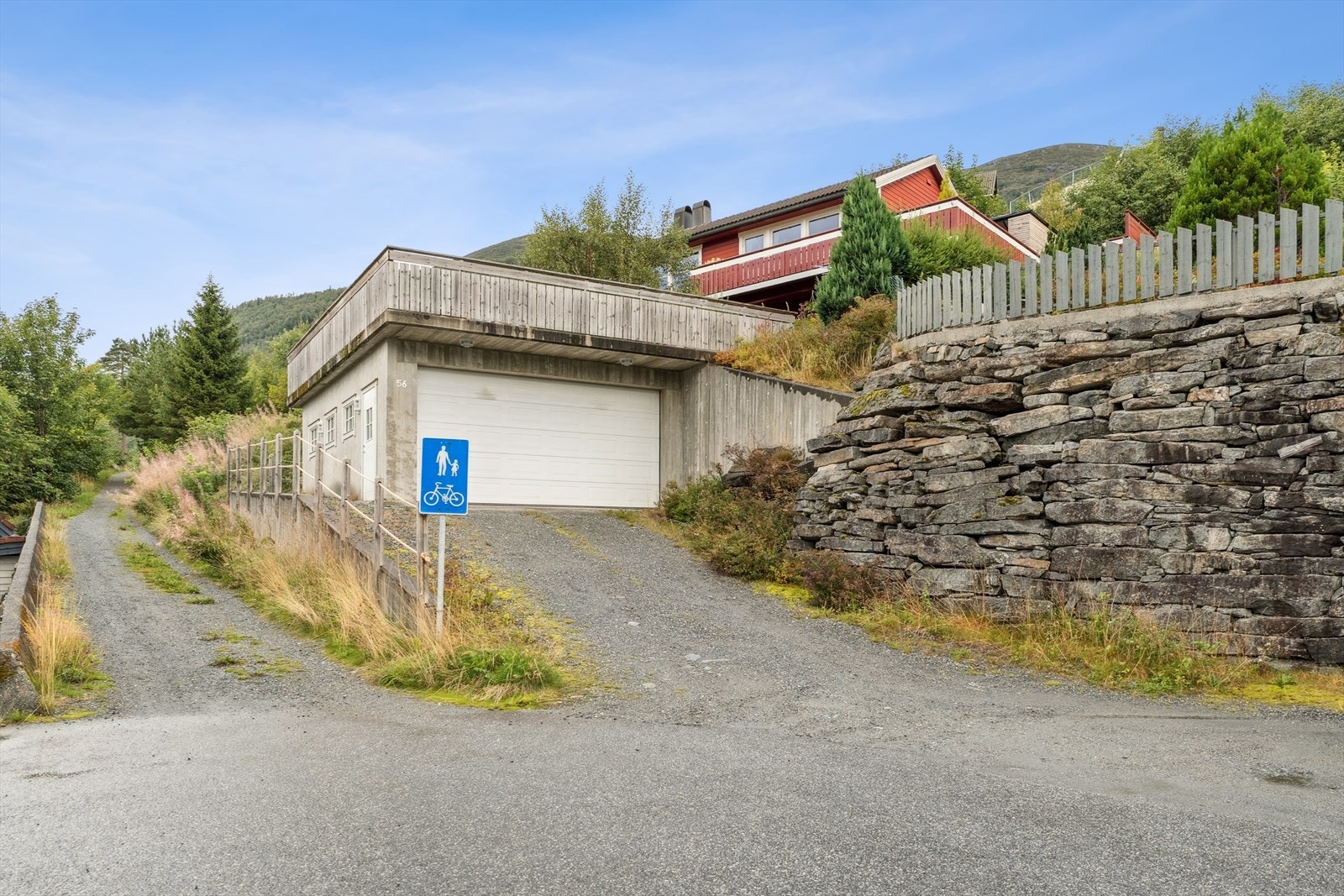 Oppkøyrsle til garasje med grus. Elektrisk garasjeport. Oppgang til husvære på sida og opp bak garasje. Galleribilde