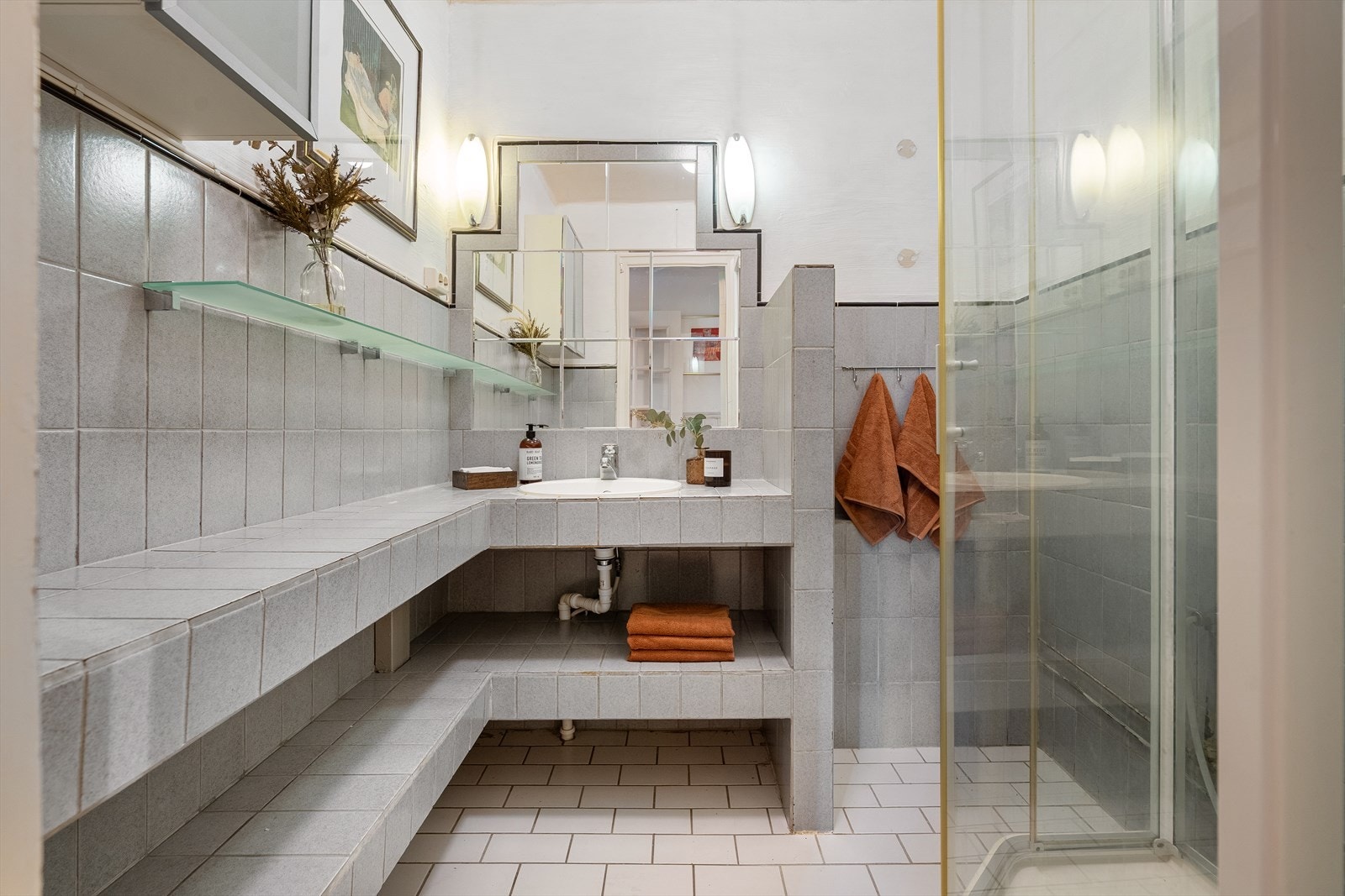 Flislagt bad som er innredet med dusjkabinett natulig ventilering, flislagt benkeplate med hvit servant og blandebatteri. Galleribilde