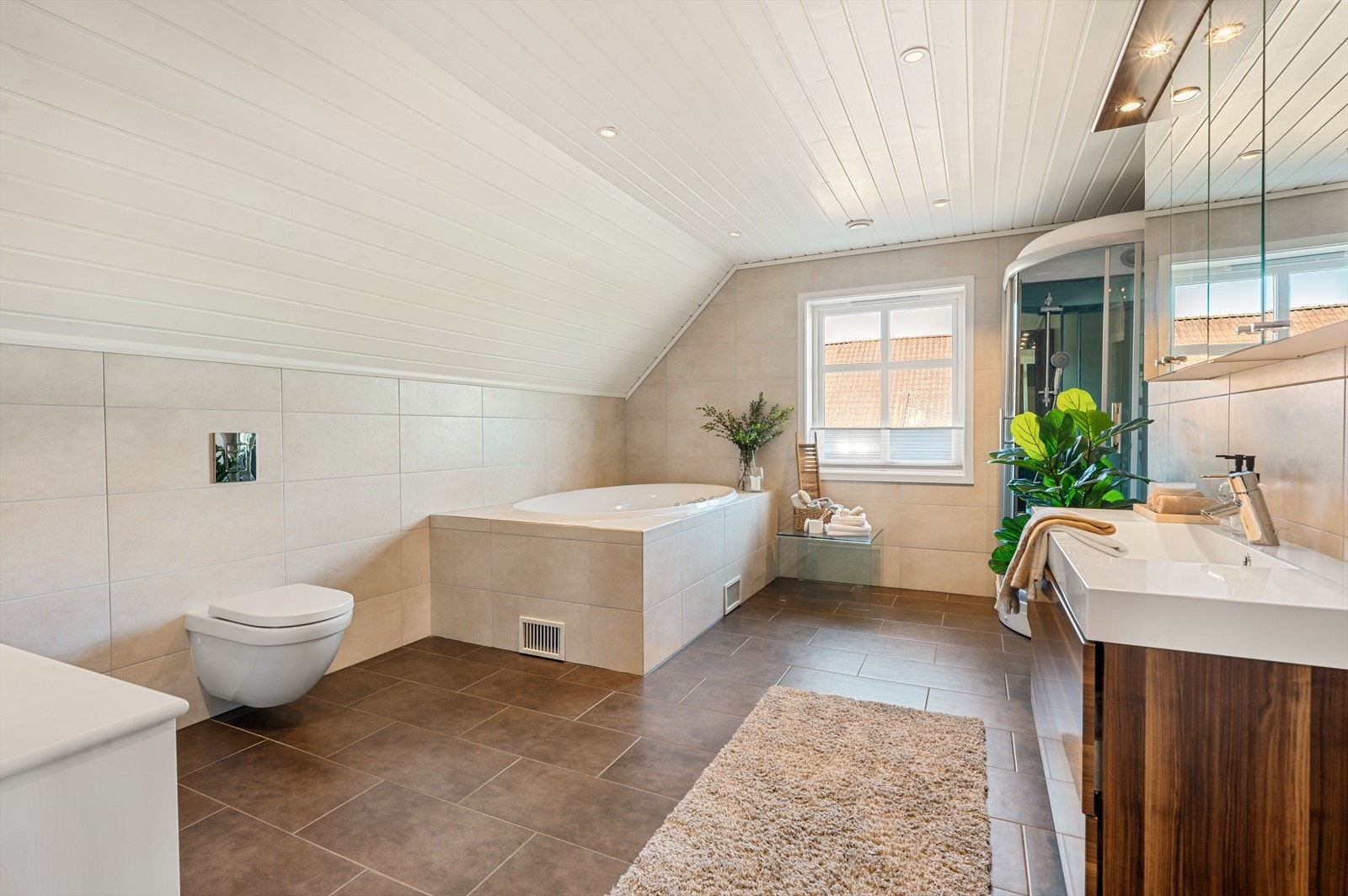 Badet er innredet med dusjkabinett, innmurt badekar, vask i seksjon. speil med belysning og vegghengt toalett. Galleribilde