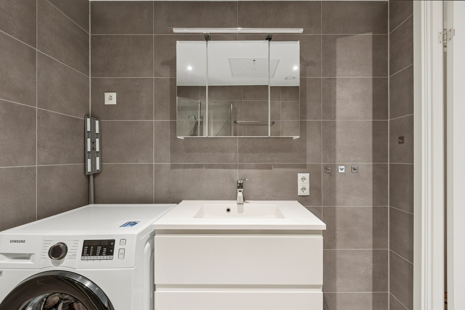 Her er det opplegg til både vaskemaskin og tørketrommel. Baderomsinnredningen har servantskap, speilskap og lys over speilet. Galleribilde