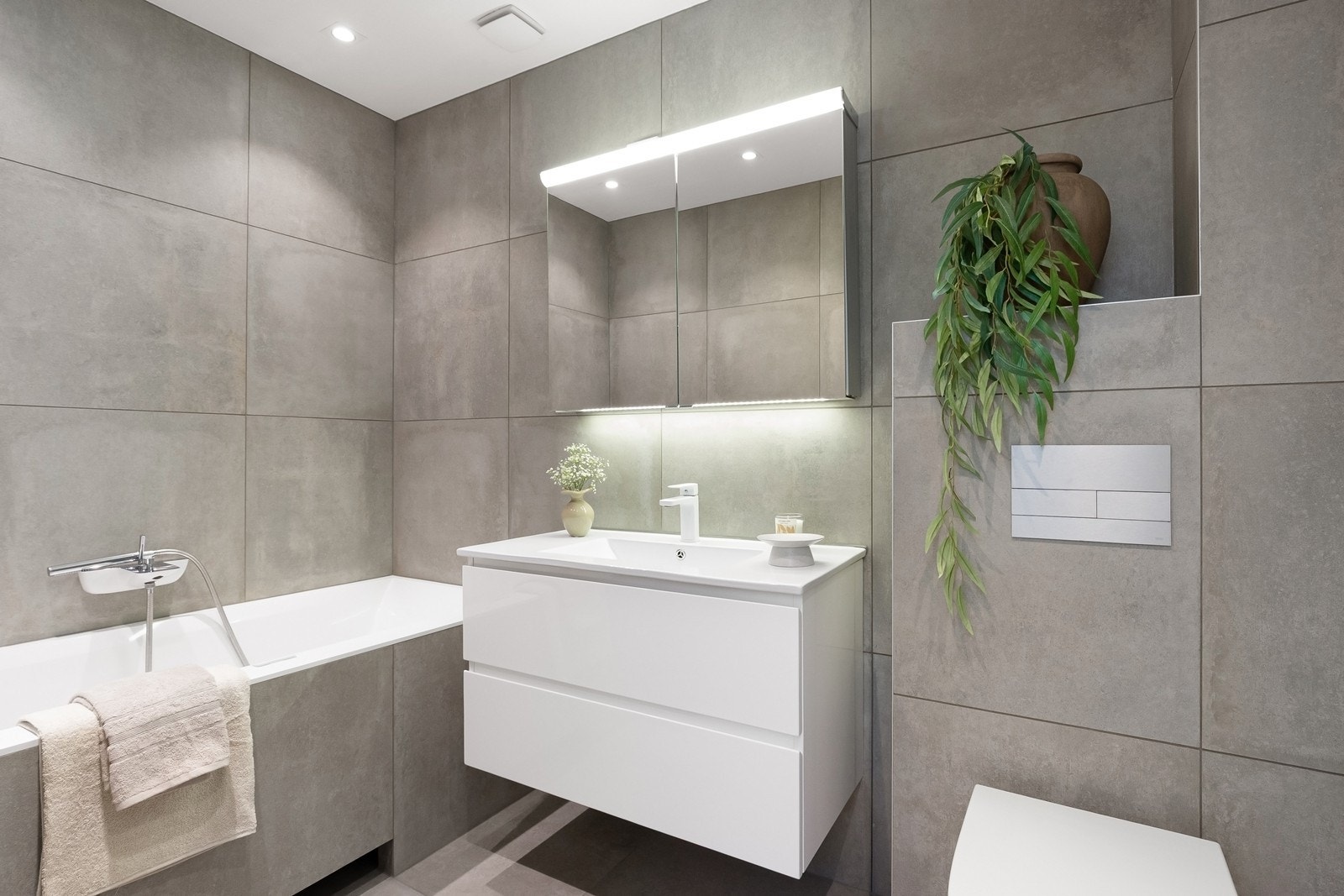 Innbydende og lekkert bad med moderne flisvalg og varme i gulv. Badet er utstyrt med plassbygd badekar, hvit skuffeinnredning, speilskap på vegg og vegghengt toalett Galleribilde