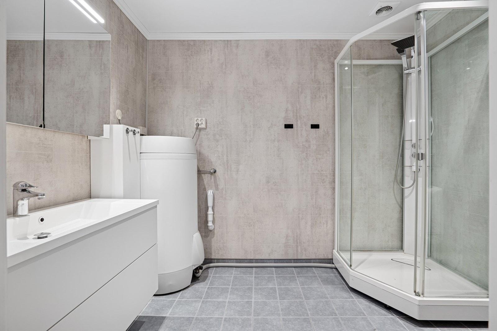 Det er montert innredning med hvite fronter og heldekkende servant, speil med integrert belysning, toalett, varmtvannsbereder og dusjkabinett. Galleribilde