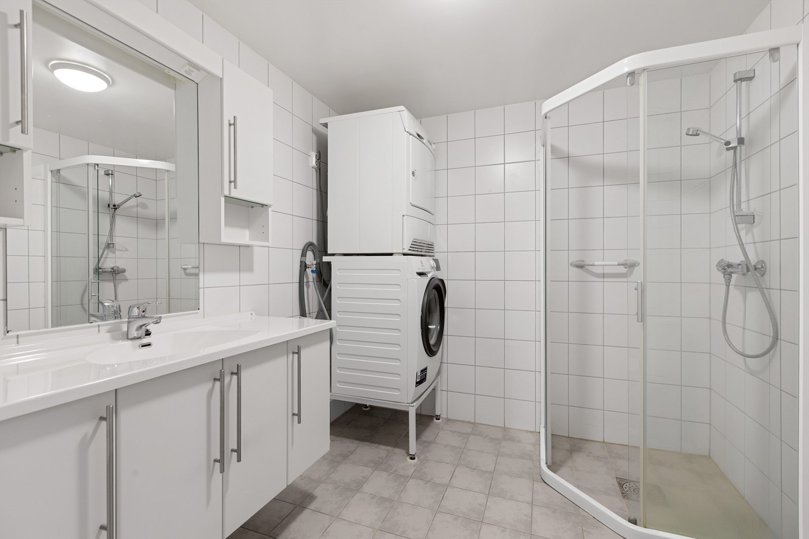 Baderom med flislagte gulv og vegger. Badet er utstyrt med servant med skap, dusjnisje med kabinett og opplegg for vaskemaskin. Galleribilde