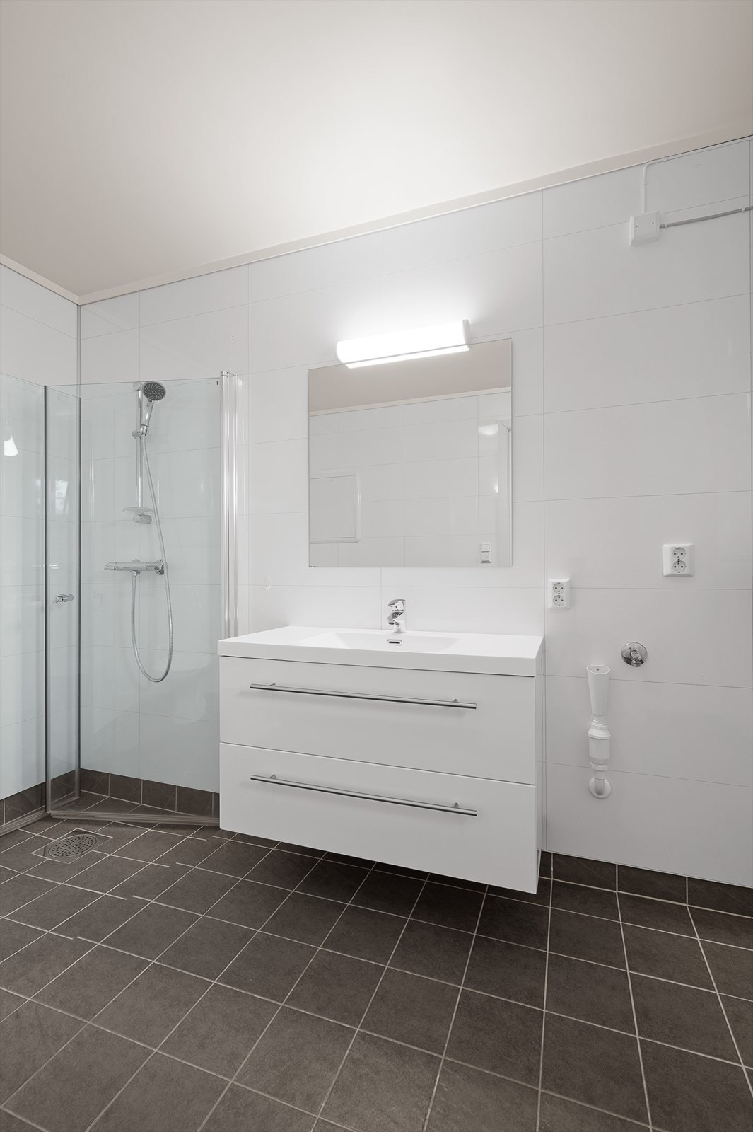 Pent, moderne bad. Flislagt gulv med varmekabler, våtromspanel på vegg og malt himling. Servant i seksjon, wc, dusjhjørne og opplegg til vaskemaskin. Galleribilde