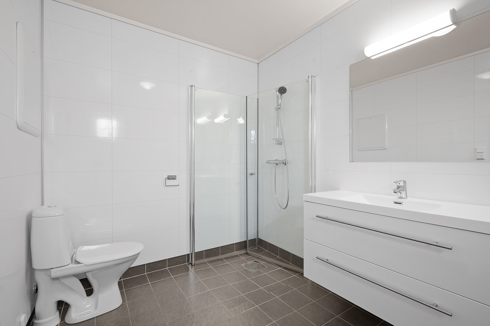 Pent, moderne bad. Flislagt gulv med varmekabler, våtromspanel på vegg og malt himling. Servant i seksjon, wc, dusjhjørne og opplegg til vaskemaskin. Galleribilde