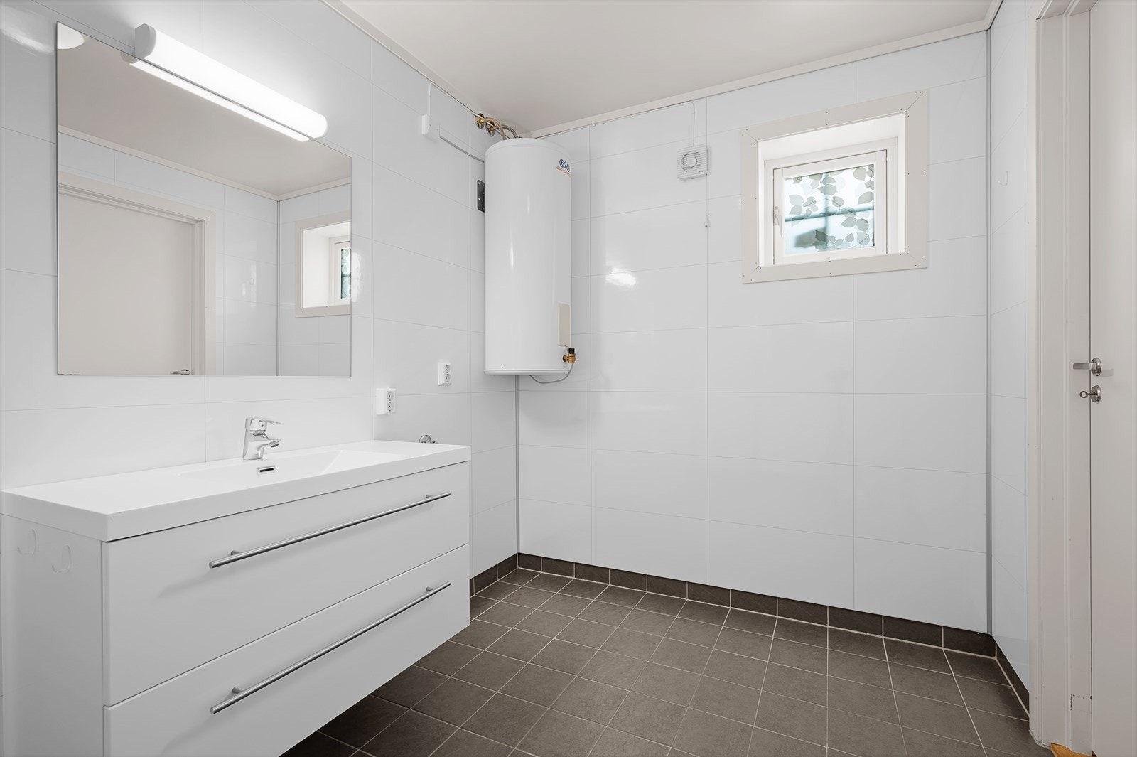 Pent, moderne bad. Flislagt gulv med varmekabler, våtromspanel på vegg og malt himling. Servant i seksjon, wc, dusjhjørne og opplegg til vaskemaskin. Galleribilde