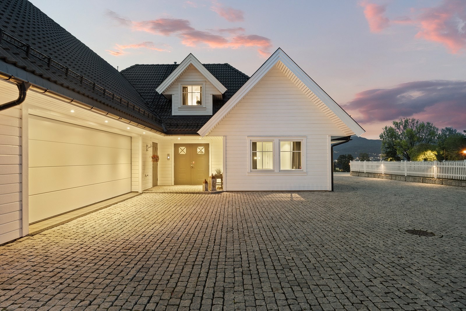 Herskapelig ankomst til romslig brosteinsgårdsplass med varme for enkelt vedlikehold vinterstid. Direkte innkjørsel til garasje med innvendig adkomst. Galleribilde