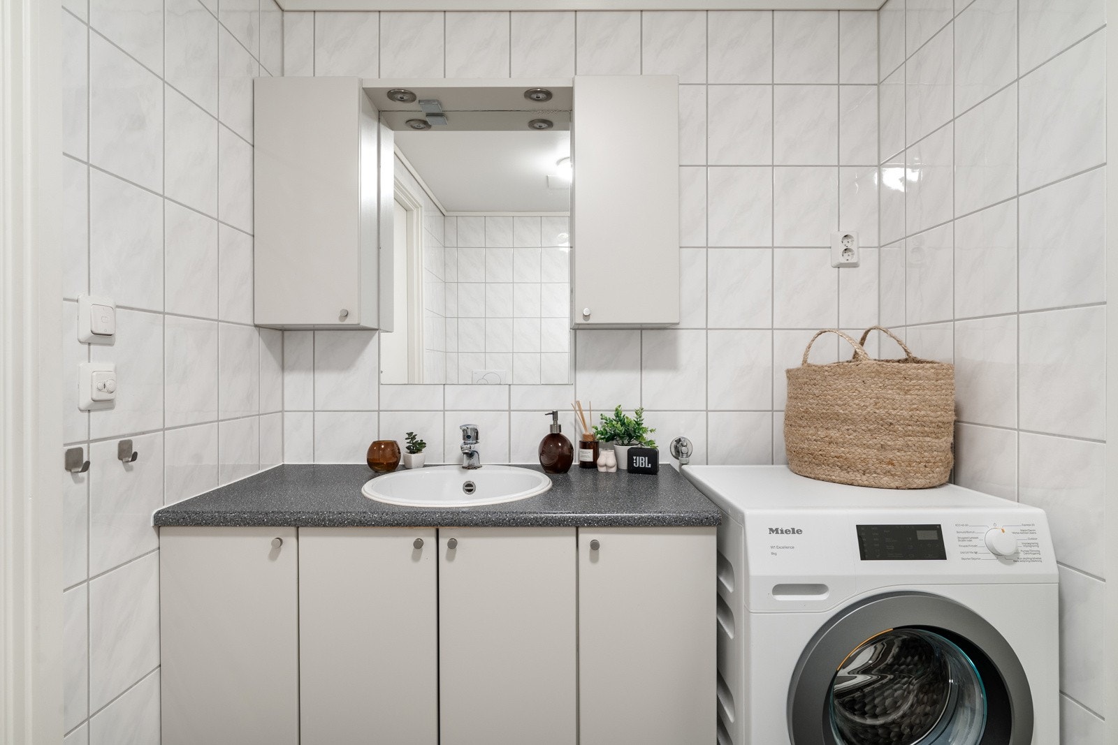 Badet er utstyrt med vegghengt toalett, dusjhjørne med innfellbare glassdører, speil og opplegg for vaskemaskin. Det er selvfølgelig behagelig varme i gulvet. Galleribilde