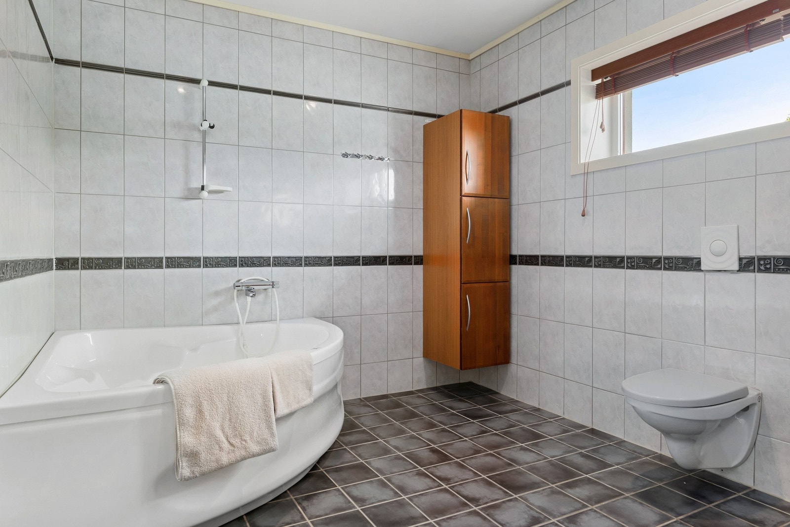 Romslig flislagt bad med badekar i hovedplan. Galleribilde