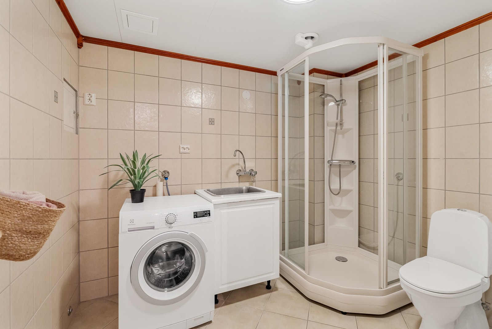 Flislagt bad/vaskerom med varmekabler i gulvet. Rommet har innredning med nedfelt servant, toalett, dusjkabinett og opplegg for vaskemaskin. Galleribilde