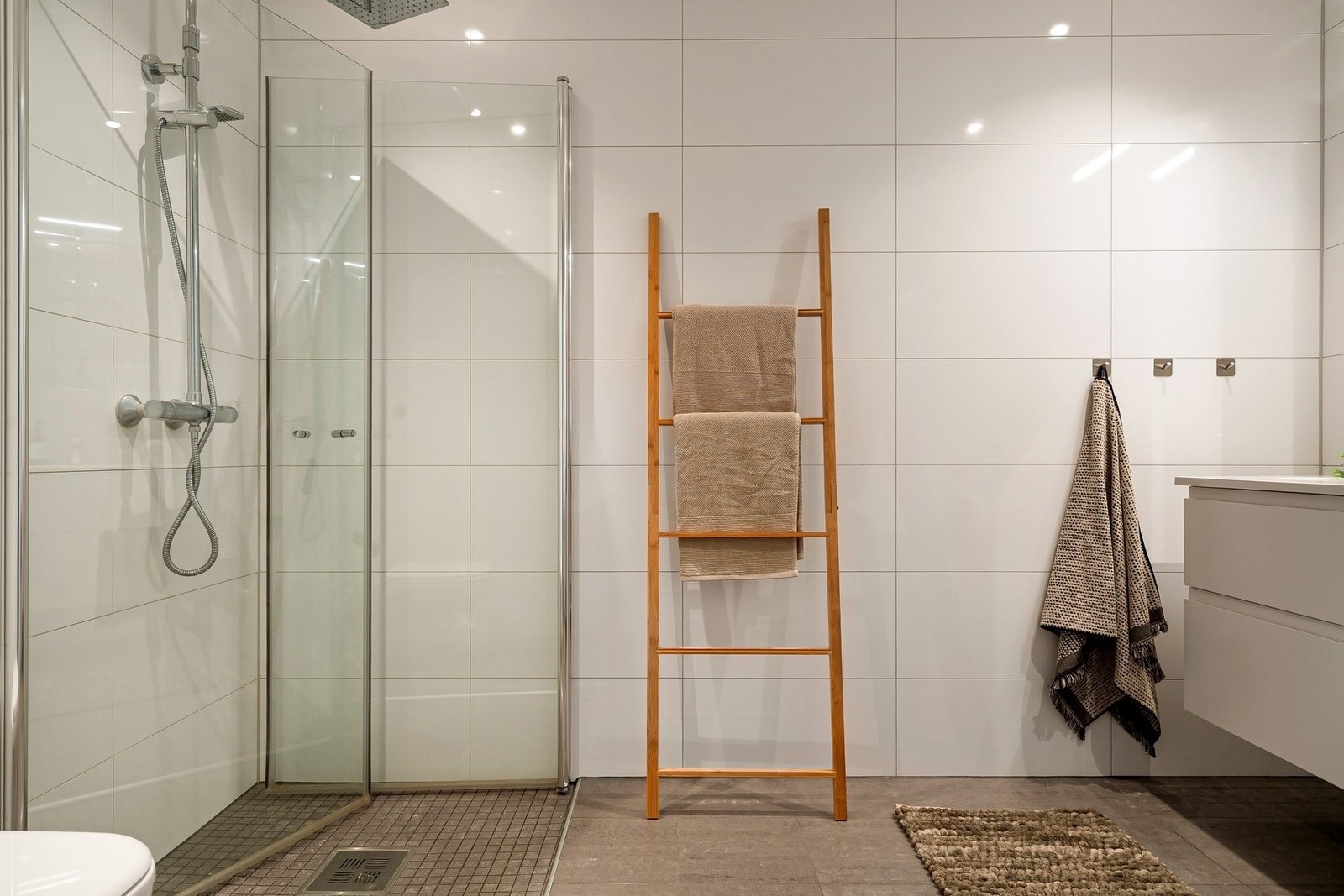 Flislagt bad med tidløst design, dusjhjørne med innfellbare glassdører og veggmontert wc Galleribilde