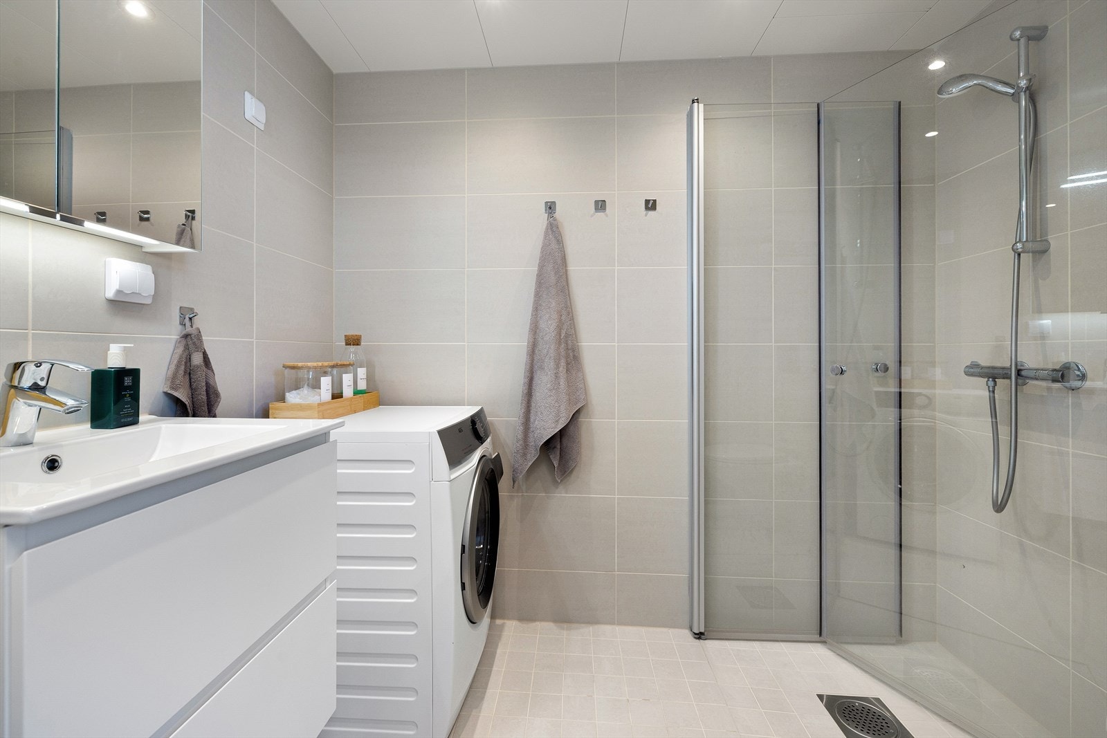 Pent flislagt bad med opplegg for vaskemaskin. Badet har flislagte overflater, vannbåren gulvvarme og downlights i taket Galleribilde