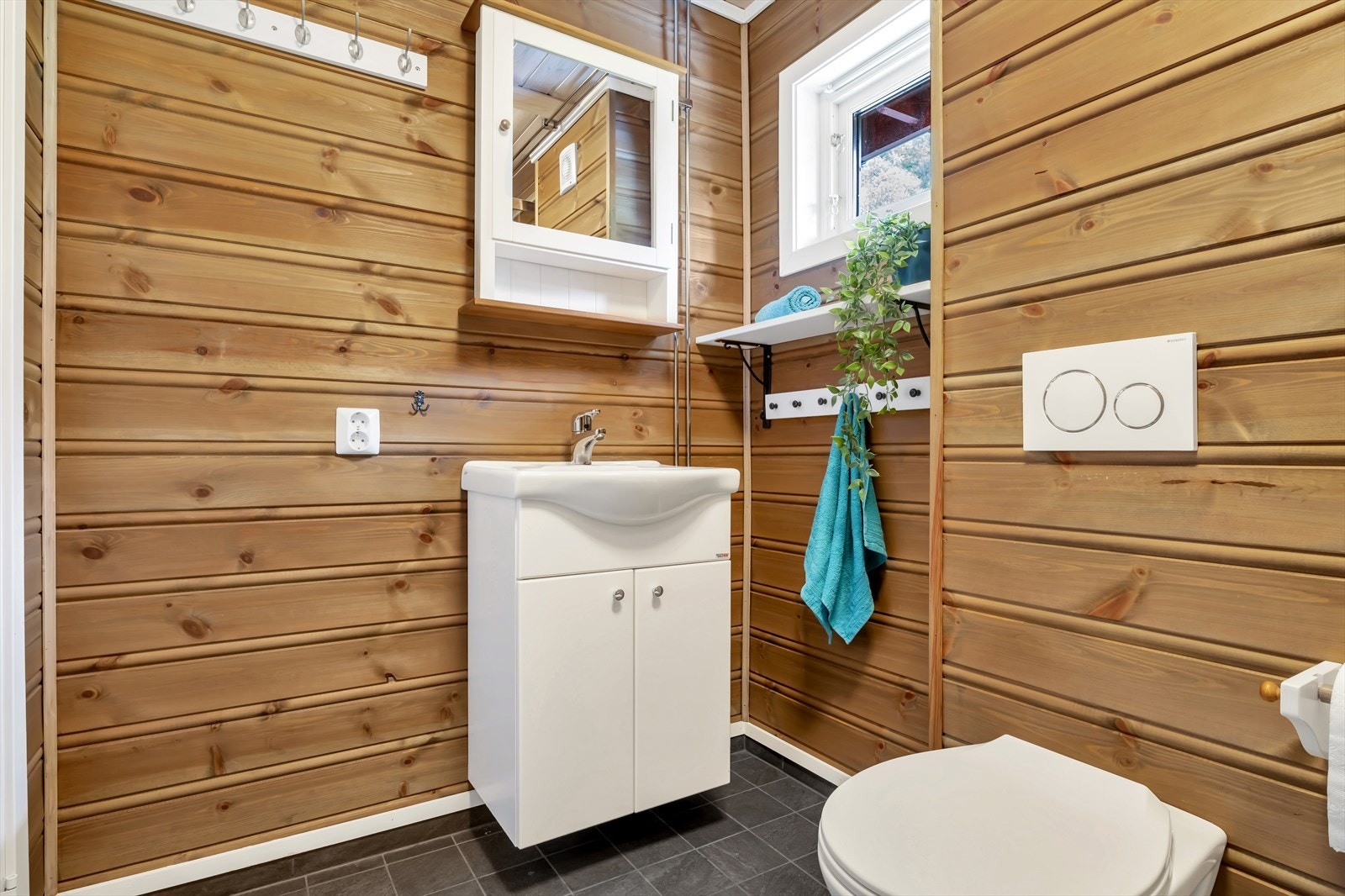 Badet er utstyrt med vegghengt toalett, dusjkabinett og benkskap med nedfelt servant, speil med belysning over. Galleribilde