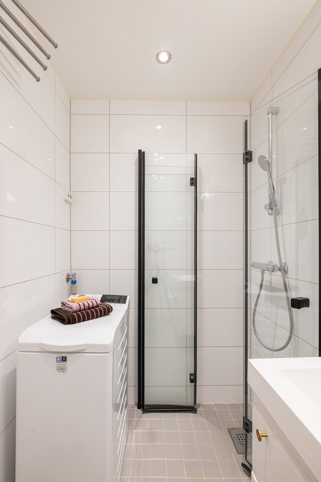 Badet er innredet med servant i skuffeseksjon for oppbevaring og veggmontert toalett. Videre er det dusjhjørne med innfellbare glassdører. Galleribilde