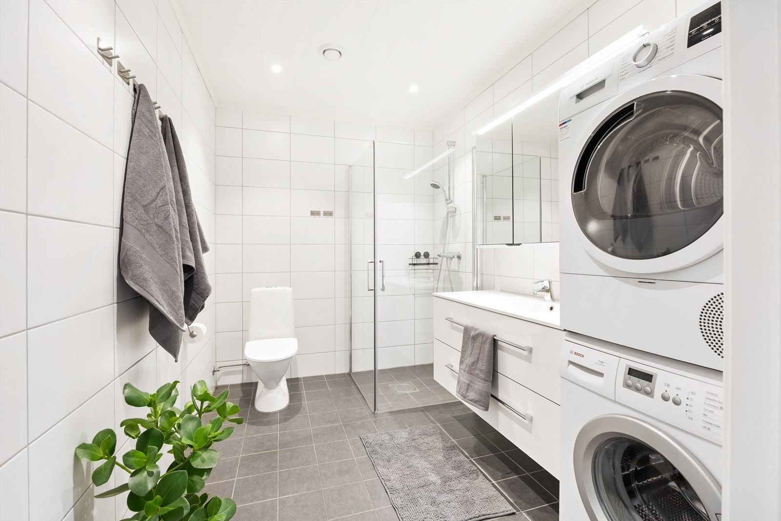 Badet er helfliset med mørke gulvfliser og hvite veggfliser, og har varme i gulvet. Galleribilde