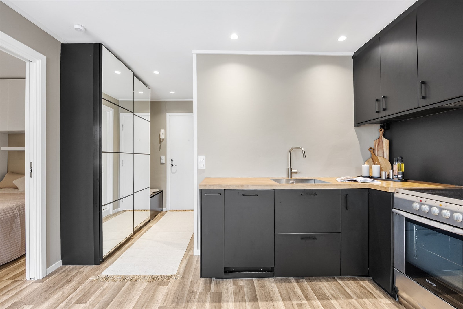 Lyst og moderne kjøkken med stilrene, sorte fronter og laminert benkeplate i tre. Godt med skap- og benkeplass, integrert oppvaskmaskin og komfyr. Galleribilde