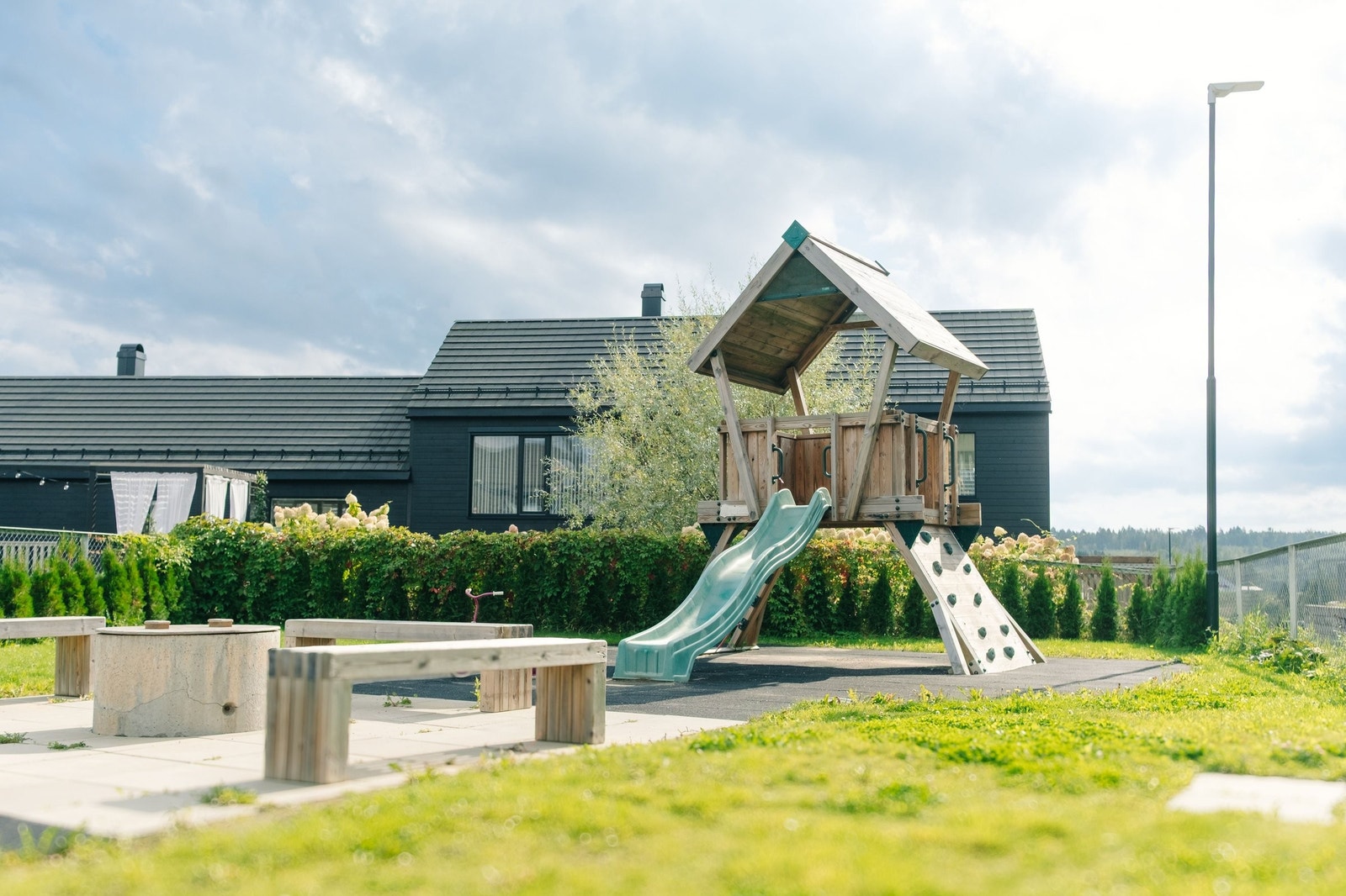 Sameiets fellesområde med inngjerdet lekeplass med klatrestativ og sosial bålplass. Galleribilde