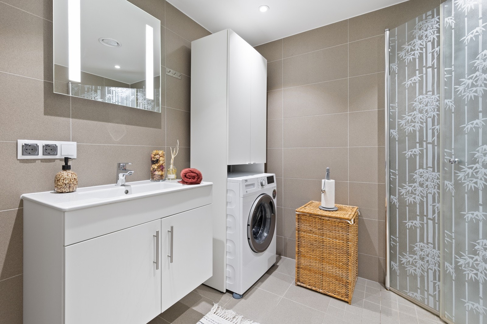 Smakfullt bad med flislagte overflater og vannbåren varme i gulv. Innredningen består av moderne skapinnredning med heldekkende hvit blank vask og vegghengt speil med integrert LED lys. Videre er det vegghengt toalett i hvitt porselen med dempesete. Galleribilde