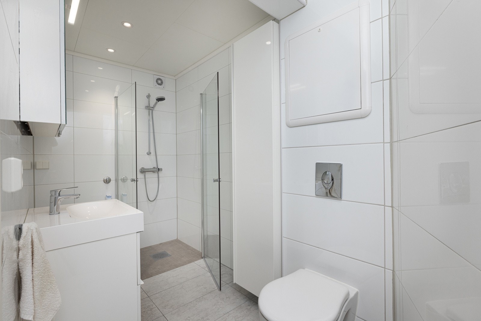 Badet fremstår tidløst og moderne med servant med underskap, speilskap, veggmontert toalett og dusjhjørne med innfellbare dører. Galleribilde