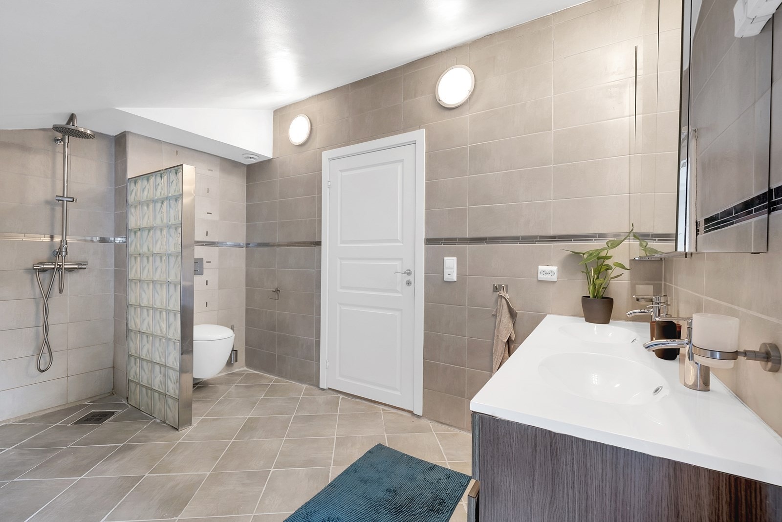 Badet er innredet med innredning med nedfelt servant, veggmontert toalett og dusjvegger/hjørne. Galleribilde