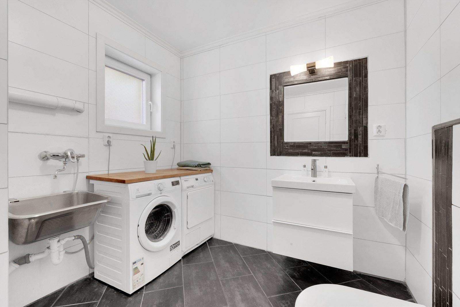 Lyst bad med elektriske varmekabler. Badet er innredet med innredning, utslagsvask, toalett og opplegg for vaskemaskin. Galleribilde