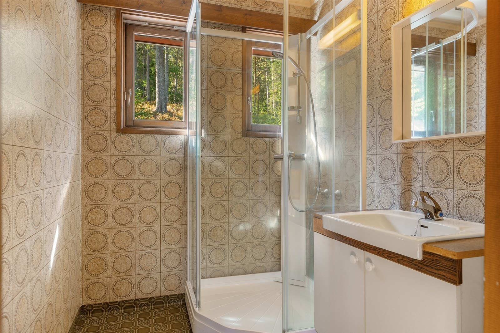 På badet, som er fra byggeår, er det belegg på vegger og på gulv. Det er montert baderomsinnredning av laminerte plater og benkeservant, samt frittstående dusjkabinett i hjørne. Galleribilde