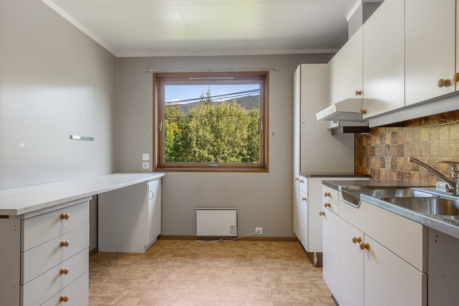 Benkeplater av laminat, og vaskebeslag av stål med nedfelt oppvaskkum og skyllekum. Kjøkkenet har ventilator med avtrekk ut. Galleribilde